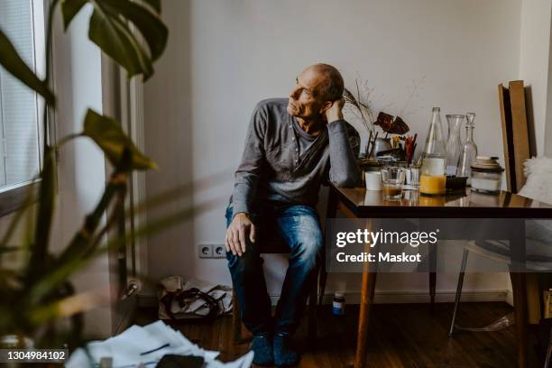 thoughtful senior man sitting on chair in living room - sadness man stock pictures, royalty-free photos & images