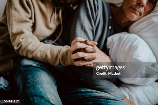 daughter holding father's hand in bedroom at home - father and grown up daughter stock pictures, royalty-free photos & images