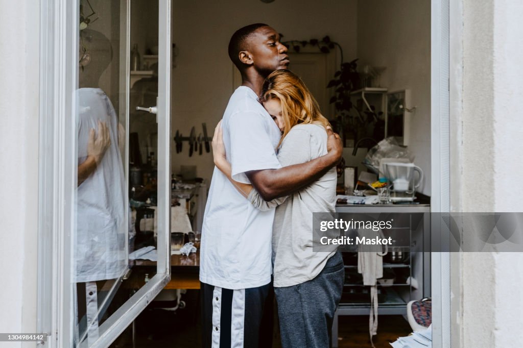 Son consoling depressed mother seen through window at home