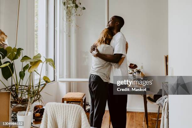 mother embracing son while standing in living room at home - consolando fotografías e imágenes de stock