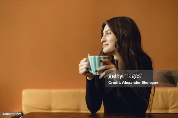 portrait of young girl on yellow background with copy space. concept with hot beverage place for text or design. she is drinking a coffee - hot arabic girl stock pictures, royalty-free photos & images