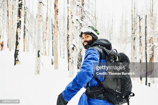 portrait of smiling snowboarder traveling through snow covered burned forest on winter afternoon - wintersport foto e immagini stock