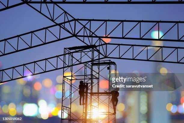 silhouette of two construction workers climbing scaffolding at night, thailand - silouhette construction work stock-fotos und bilder