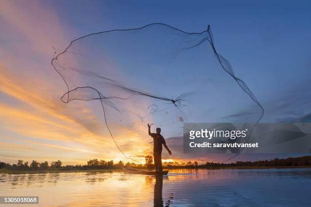 silhouette of a fisherman throwing a fishing net into river, thailand - pesca de lançamento imagens e fotografias de stock
