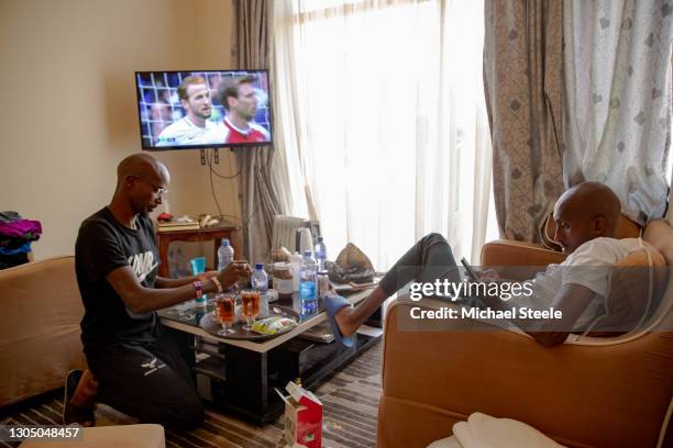 Mo Farah stirs a cup of tea alongside room mate and training partner Abdi Abdirahman as the Arsenal v Tottenham Hotspur football game plays out on...