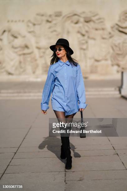 Michelle Wehbe, actress, wears a black hat, sunglasses, a blue long shirt worn as a dress, a black bag, black tights, black thigh high pointy boots,...