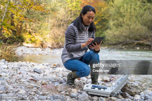 japanse vrouwelijke onderzoeker die waterkwaliteit in aard test. vrouw die draadloze digitale tablet met behulp van. - biologist stockfoto's en -beelden