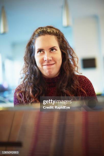 curly-haired young woman looks pleased and smug, sitting at her laptop computer at home - pleased face laptop stock pictures, royalty-free photos & images