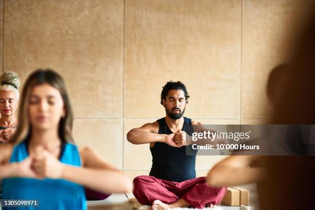 man sitting cross-legged in yoga studio - yoga studio stock pictures, royalty-free photos & images