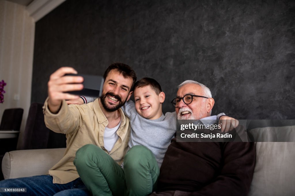 Smiling boys are sitting on sofa bed and taking selfie.