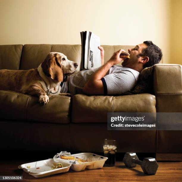 man laying down on sofa eating food. - dog looking down stock pictures, royalty-free photos & images