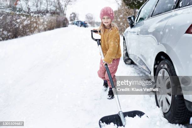 girl removing snow with shovel by car at driveway - snow shovel stock pictures, royalty-free photos & images