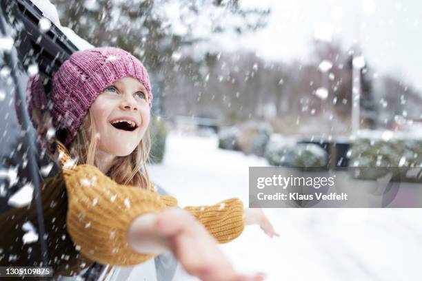 happy girl enjoying snowfall through car window - winter car window stock-fotos und bilder