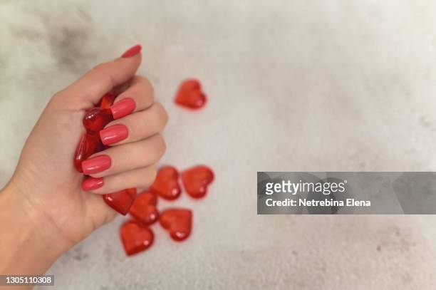 a beautiful woman's hand with a red manicure holds hearts in her hand on a light background. space for the text. copy-space - clear skin red background stock pictures, royalty-free photos & images
