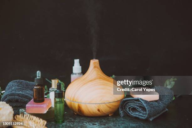 electric essential oils aroma diffuser, oil bottles and flowers on gray surface with reflection. - aromatherapy stock pictures, royalty-free photos & images