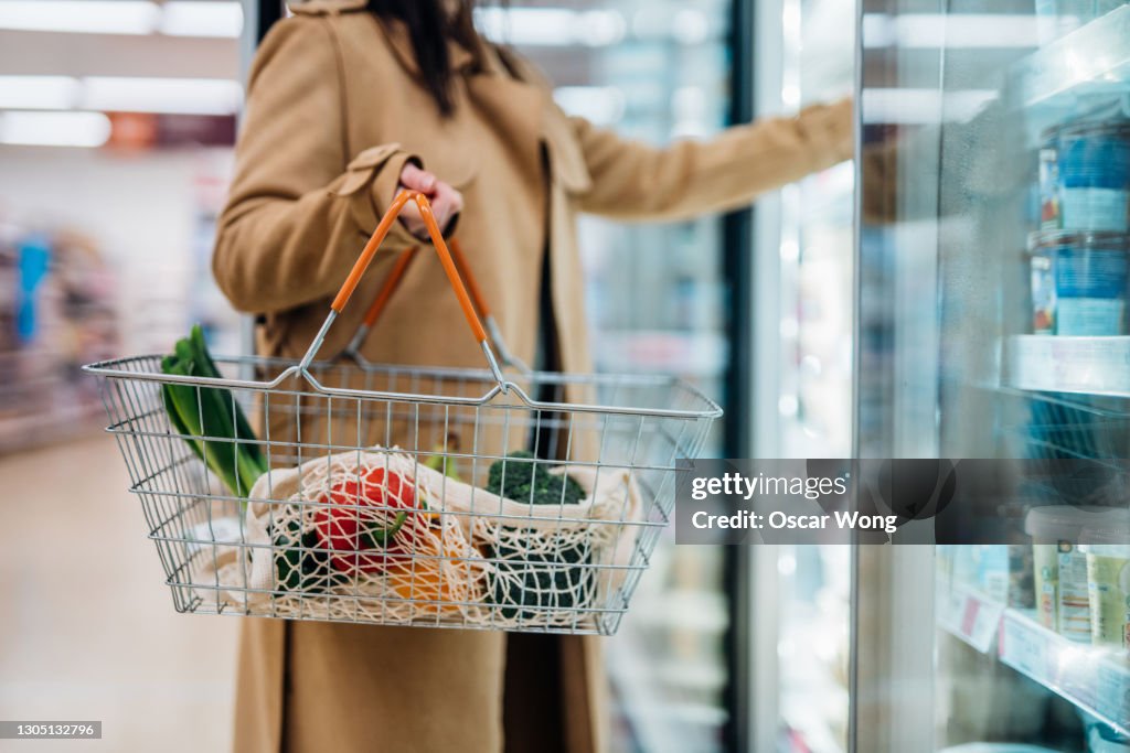 Cropped shot of woman carrying shopping basket and shopping groceries in supermarket