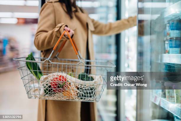 cropped shot of woman carrying shopping basket and shopping groceries in supermarket - frozen food stock pictures, royalty-free photos & images