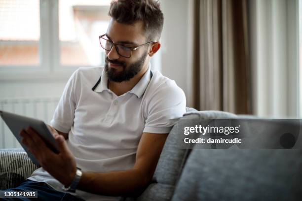 smiling young man using digital tablet at home - subscription stock pictures, royalty-free photos & images