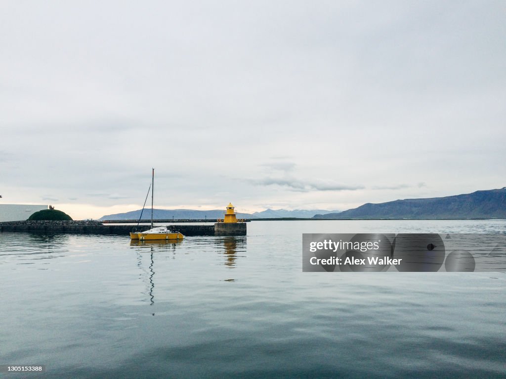 Small yellow lighthouse and sailboat on coastal wall