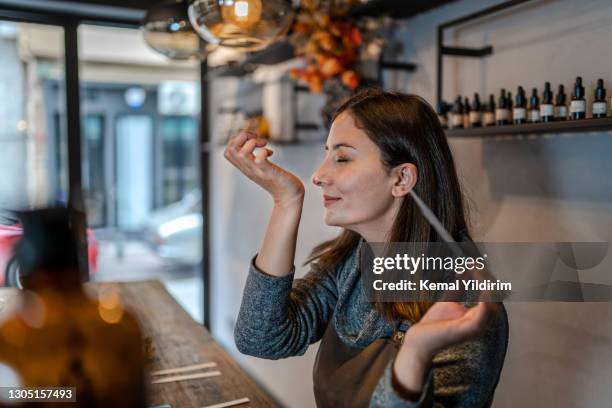 joven perfumista preparando perfume mientras se sienta a la mesa en su propia tienda - perfumería fotografías e imágenes de stock