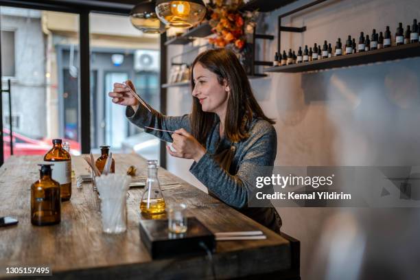 giovane profumiere che prepara il profumo mentre è seduto a tavola nel suo negozio - profumato foto e immagini stock