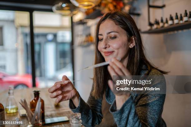 joven perfumista preparando perfume mientras se sienta a la mesa en su propia tienda - perfumería fotografías e imágenes de stock