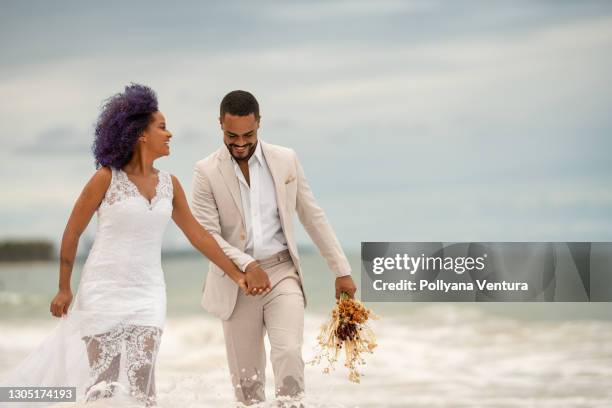 novio y novia caminando en el borde del mar - matrimonio fotografías e imágenes de stock