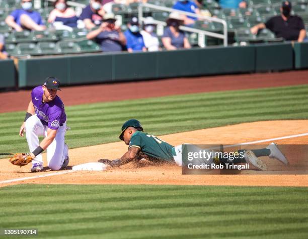 Buddy Reed of the Oakland Athletics slides safely into third base before the tag of Ryan McMahon of the Colorado Rockies during a spring training...