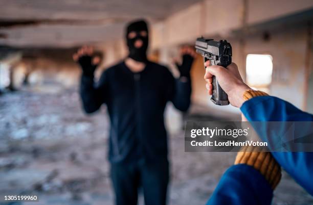 woman aiming a gun at a man in camouflage clothing - balaclava gun stock pictures, royalty-free photos & images