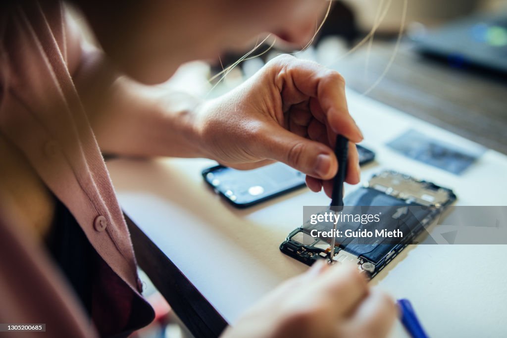 Woman repairing mobile phone at home, changing damaged part.