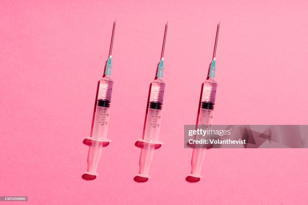 Three syringe with injection or vaccine on pink background