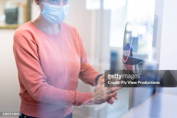 patient in medical office using hand sanitizer from automatic dispenser - soap dispenser stock pictures, royalty-free photos & images