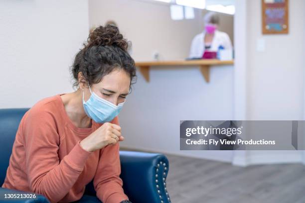 sick woman wearing protective face mask coughing while waiting in lobby of medical clinic - old cough stock pictures, royalty-free photos & images