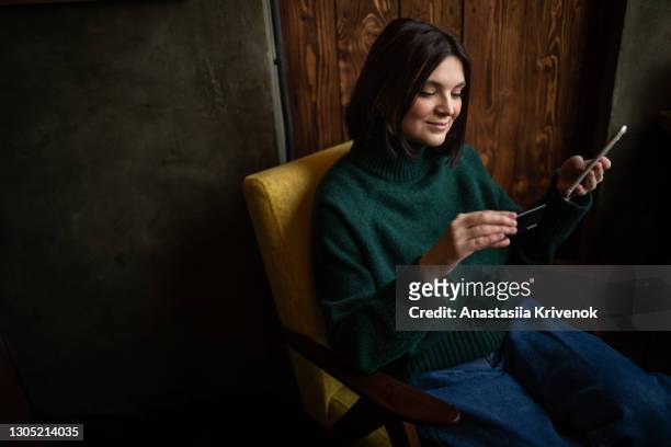 happy woman shopping online with a credit card and a phone in living room. - white smart phone stock pictures, royalty-free photos & images