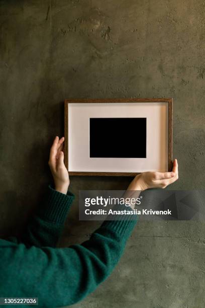 woman's hands holding and supporting picture frame on the wall. - positionner photos et images de collection