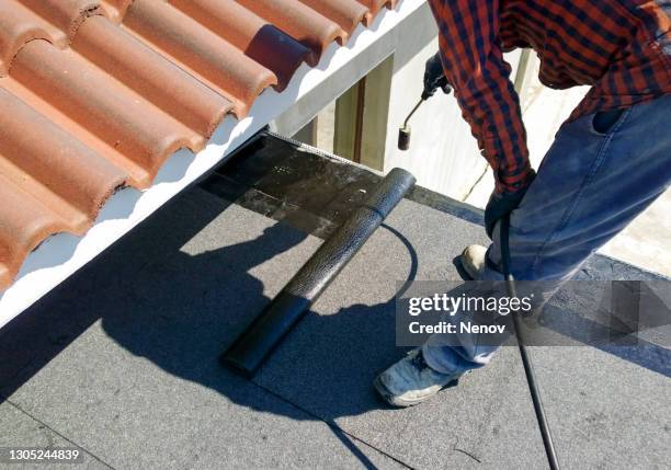 roofer preparing part of bitumen roofing felt roll for melting by gas heater torch flame - waterproofing stock pictures, royalty-free photos & images