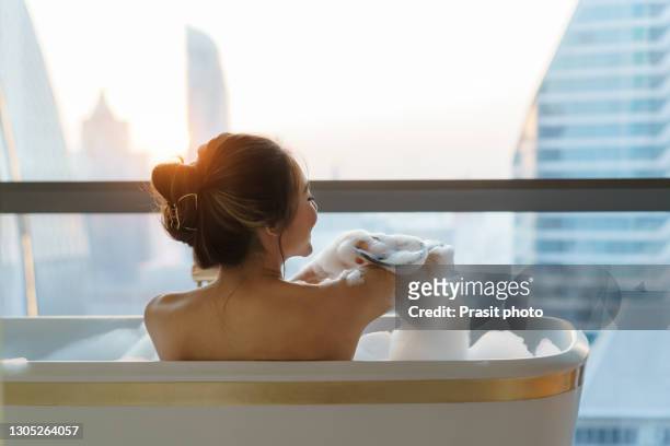 asian woman takes a bath with soap bubble in bathtub at bathroom of luxury hotel in downtown city while on vacation. - hyatt hotels corp hotel ahead of earnings figures stockfoto's en -beelden