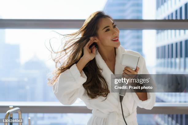 asian woman in bathrobe using a hair dryer to dry her hair in the bathroom while preparing to go to work in the morning at home or in a luxury hotel in downtown city. - hair dryer ストックフォトと画像