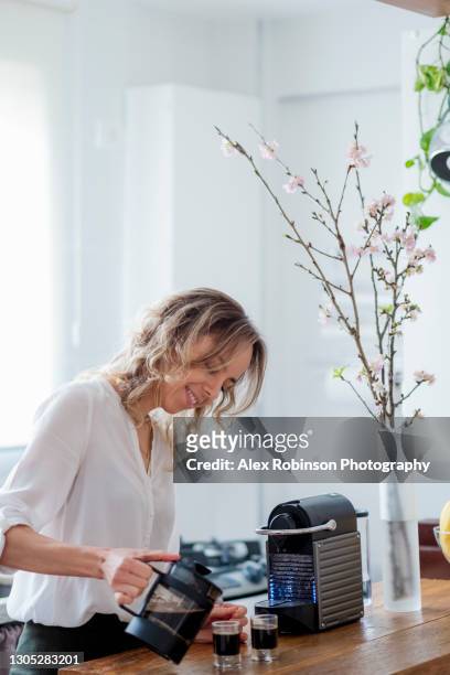 a woman in her thirties making espresso coffee at home in a modern kitchen - coffee maker - fotografias e filmes do acervo