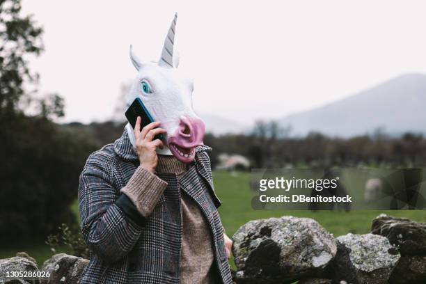 woman with unicorn latex mask in the field, talking on the mobile phone - unicorn stock pictures, royalty-free photos & images