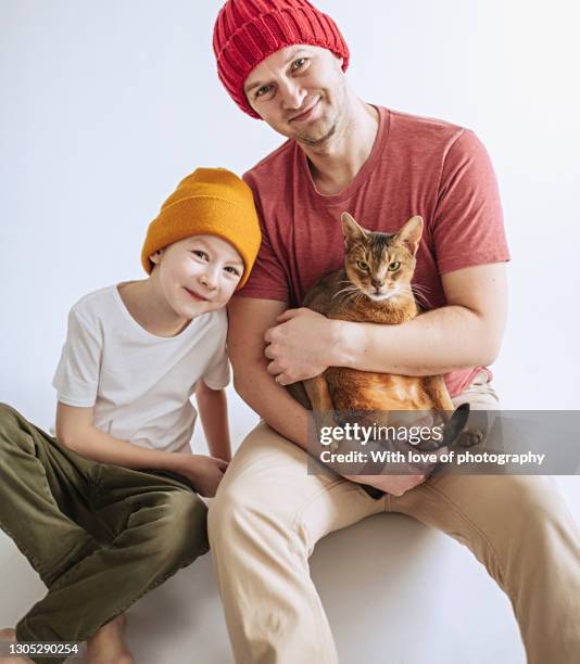 mid-adult european father with 7 year old son in bright beany hats on white background with a cat - 40 44 ans stock pictures, royalty-free photos & images