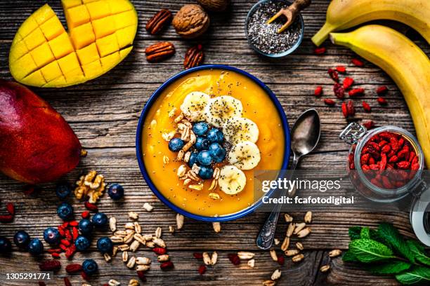 mango and banana smoothie bowl on rustic wooden table. - yellow smoothie stock pictures, royalty-free photos & images