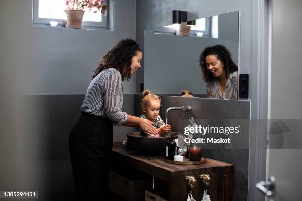 smiling woman washing hands with daughter in sink at home during pandemic - rubbing hands together stock pictures, royalty-free photos & images