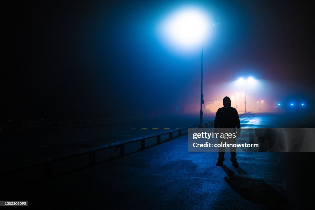 Sinister silhouette man lurking in deserted parking lot