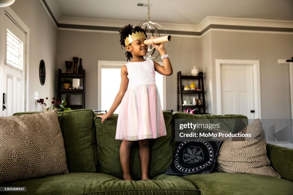 Young girl wearing homemade crown and looking through homemade telescope