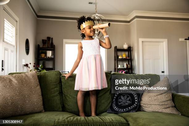 young girl wearing homemade crown and looking through homemade telescope - giochi per bambini foto e immagini stock