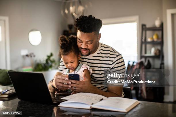 father working from home while holding toddler - gente mirando moviles fotografías e imágenes de stock