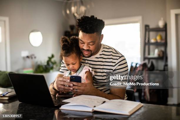 father working from home while holding toddler - black man laptop foto e immagini stock