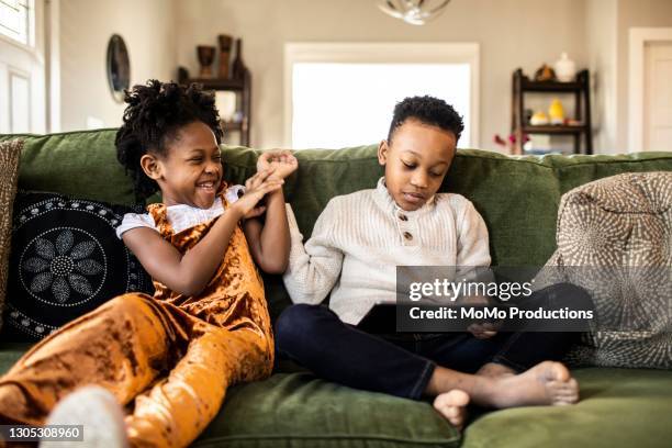 brother and sister watching digital tablet on sofa at home - rough housing stock pictures, royalty-free photos & images