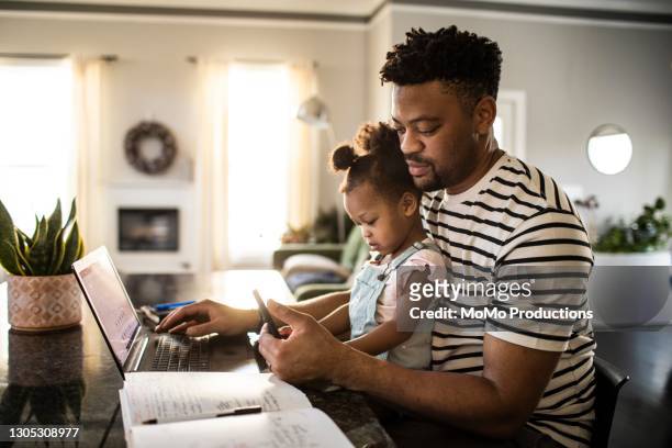 father working from home while holding toddler - african american dad stock-fotos und bilder